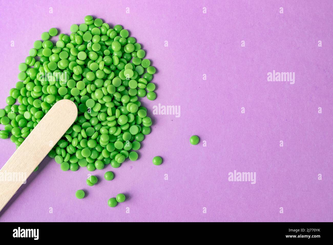 Beautiful green wax granules for depilation, and wooden spatulas on a pink background. Epilation, depilation, removal of unwanted hair. View from abov Stock Photo