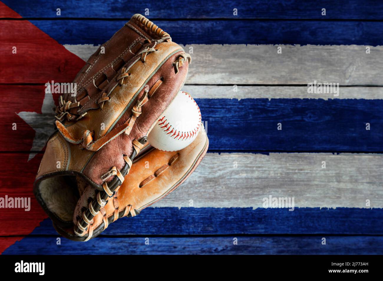 Leather baseball glove with ball on rustic wooden background with painted Cuban flag and copy space. Cuba is one of the world's top baseball nations. Stock Photo