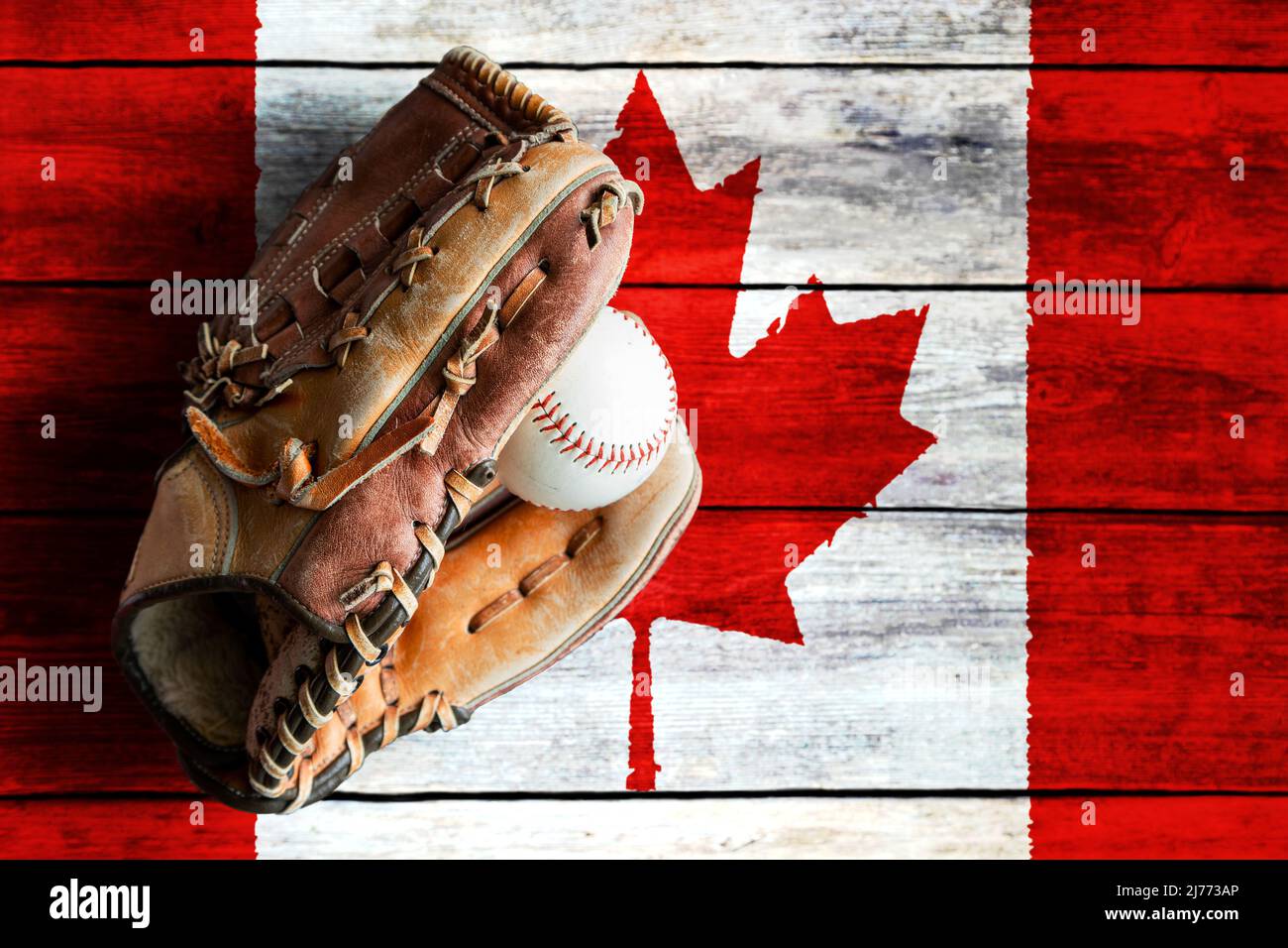 Leather baseball glove with ball on rustic wooden background with painted Canadian flag and copy space. Canada is one of the world's top baseball nati Stock Photo