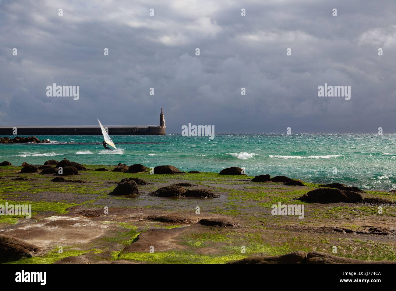 Tarifa, Spain - February 6,2022: Wind Surfer on the beach in Tarifa. Lighthouse in Tarifa and dramatic sky, Andalusia, Spain.Tarifa is one of the worl Stock Photo