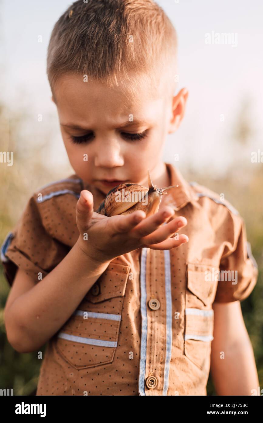 A serious little boy holds a snail in his hand in nature Stock Photo