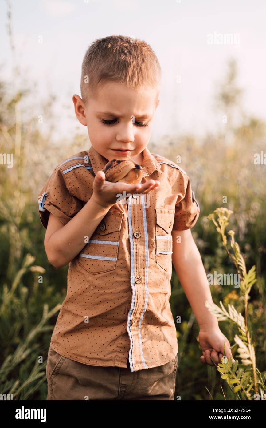 A serious little boy holds a snail in his hand in nature Stock Photo