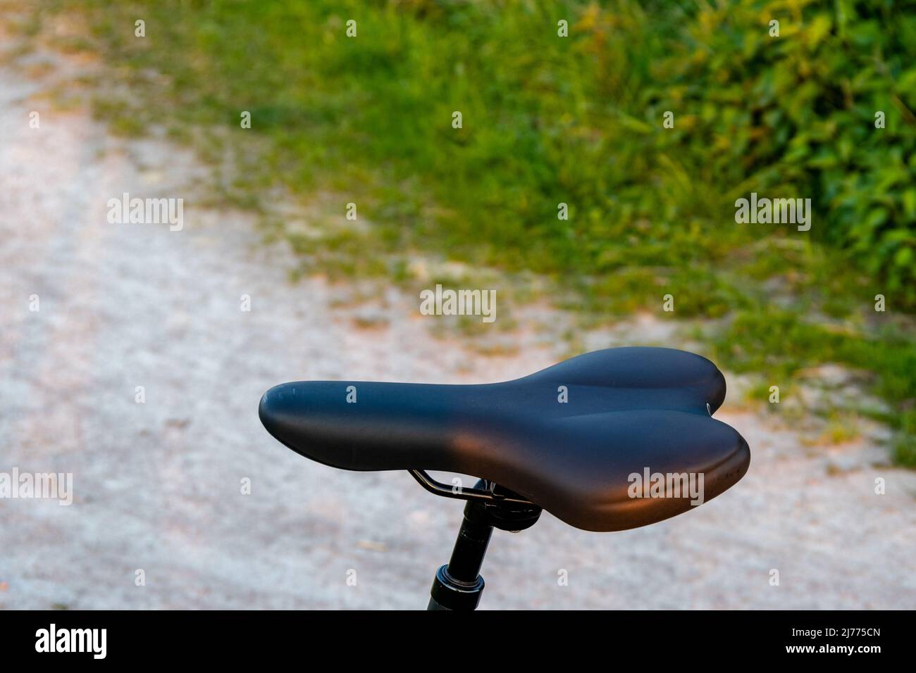 closeup of a black bicycle saddle with a blurred path and lawn in the background Stock Photo
