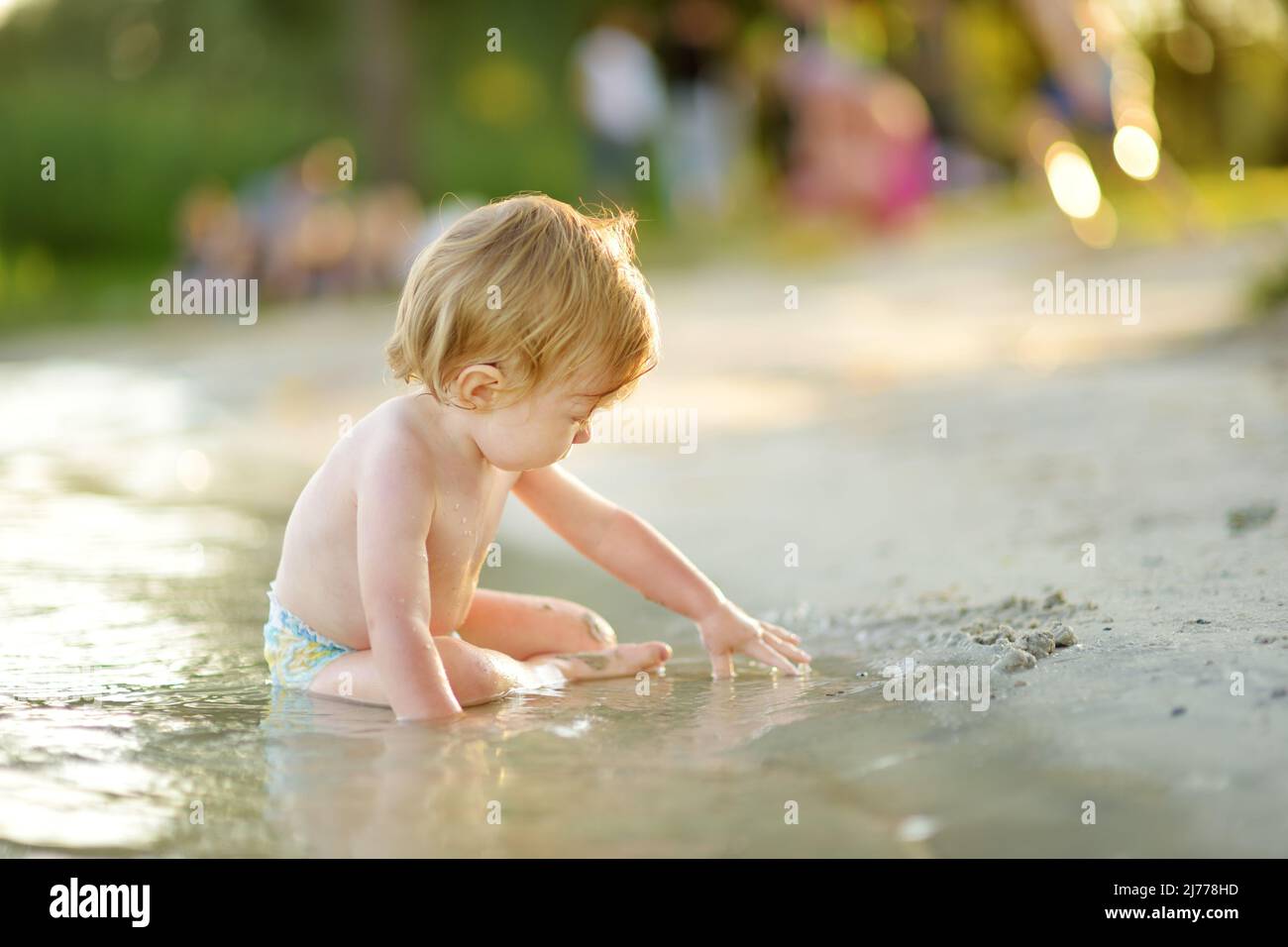 Cute toddler boy wearing swimming diaper playing by a river on hot