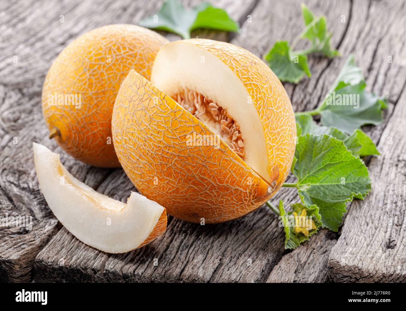 Ripe yellow melon with slices and melon leaves on a old wooden table. Stock Photo