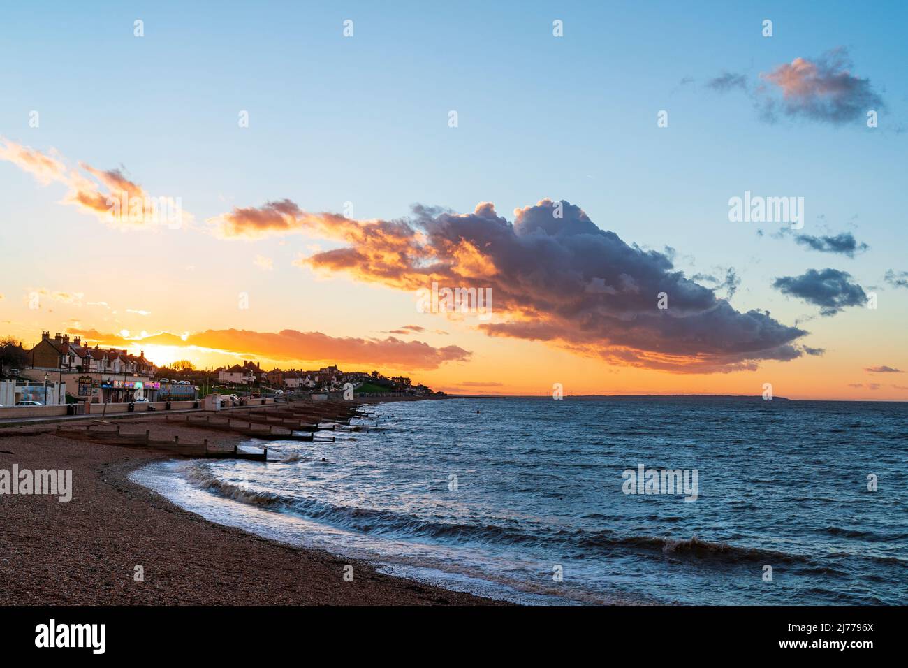 Herne Bay seafront with sunset over houses. High tide, with groynes