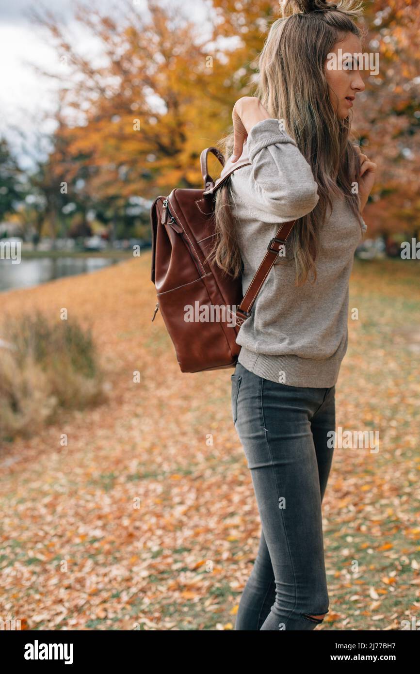 woman adjusting backpack outside in the fall surrounded by orang Stock
