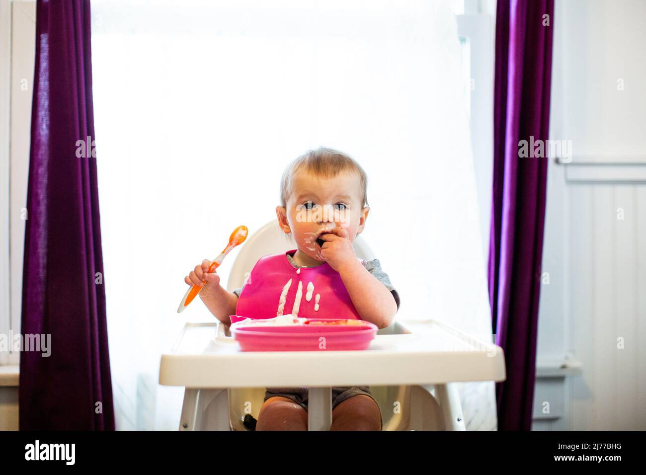 Baby in a Pink Bib Eating Yogurt Messily Stock Photo