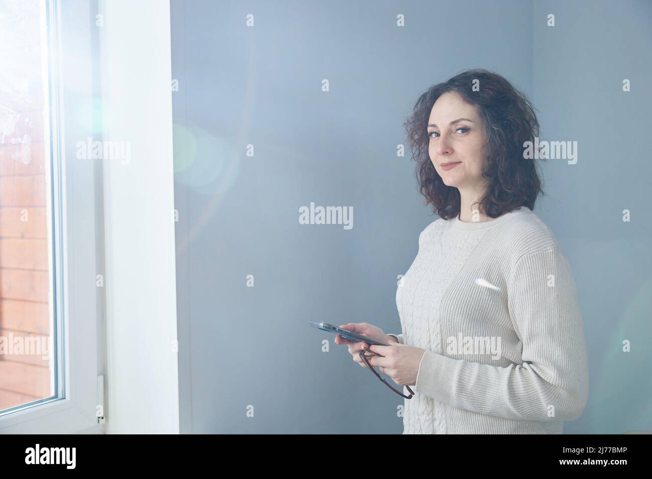 Portrait of a middle-aged brunette standing at the window phone Stock Photo