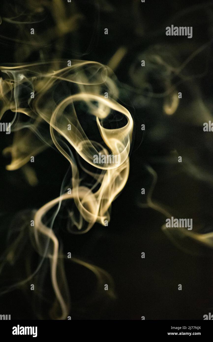 A swirling ascending smoke pattern with a yellowish gold color on a black background, photo could be used as a background, smoke texture or abstract, Stock Photo