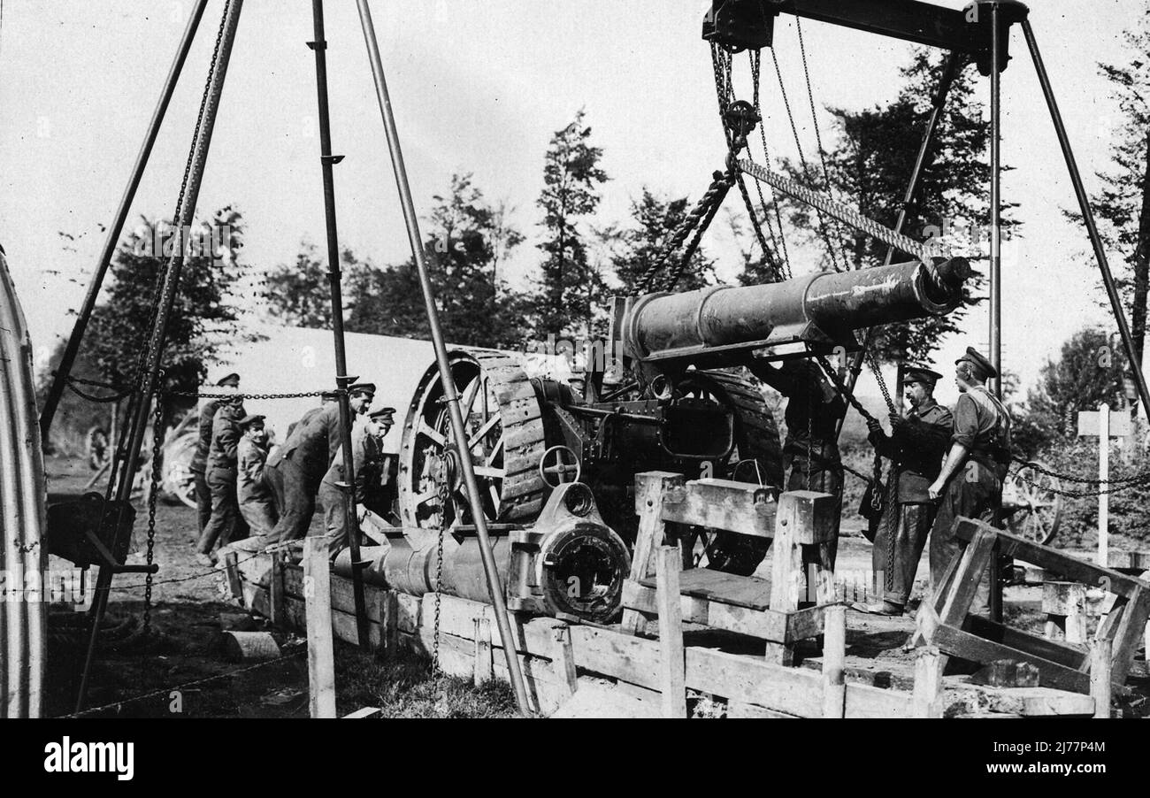 Howitzer is suspended from a hoist having just been lifted off its wooden platform. Six soldiers are straining at a lever under one of its wheels while another two are hauling on the guide chains. Stock Photo