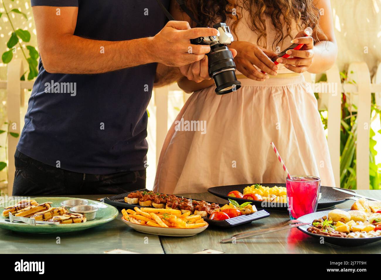 beautiful indian woman and arabian man photographing dishes in summer tropical cafe on camera Stock Photo