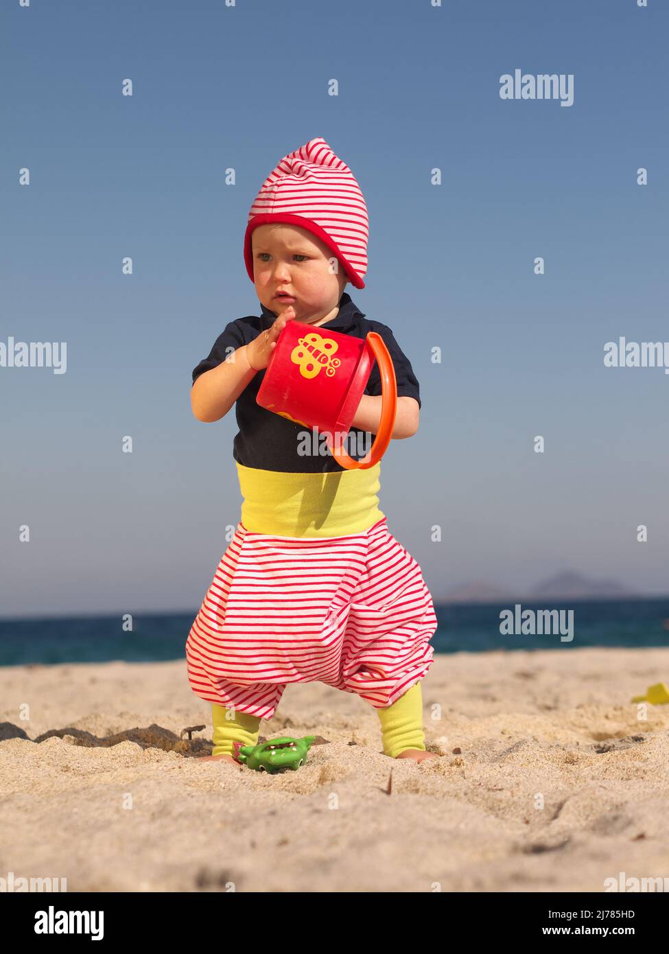 einjähriges Mädchen steht am Strand mit Eimer in der Hand Stock Photo