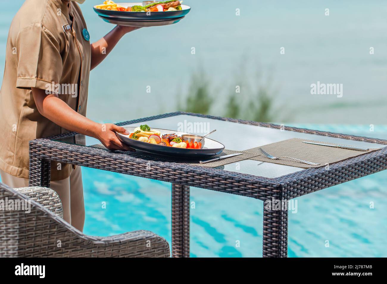 Unrecognizable waitress put food plates on table in outdoors restaurant at hotel Stock Photo