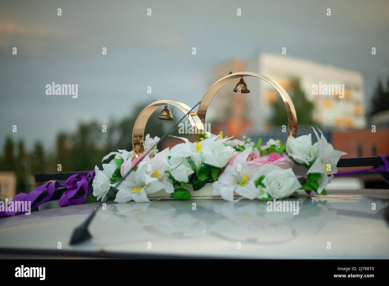 Wedding rings on roof of car. White flowers and bells adorn newlyweds