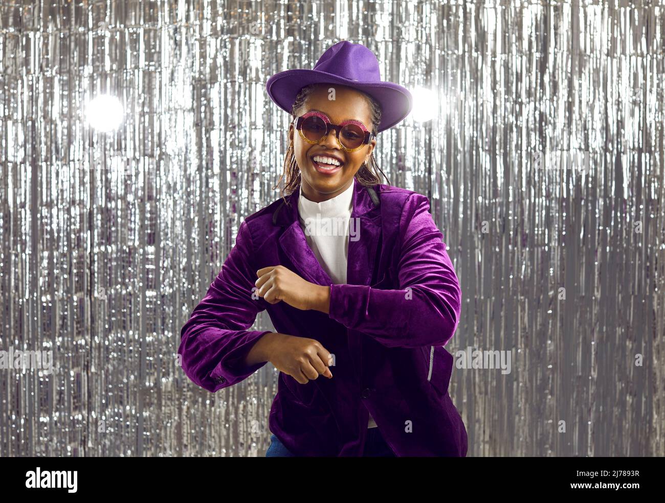 Funny extravagant young african american woman having fun dancing on shiny silver background. Stock Photo