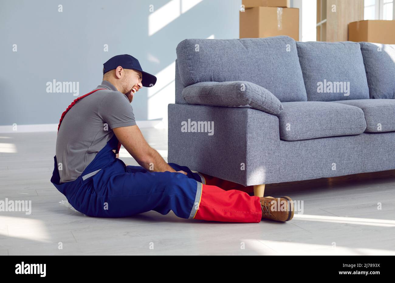 Delivery worker who lifts heavy furniture gets his foot pinned under heavy couch Stock Photo