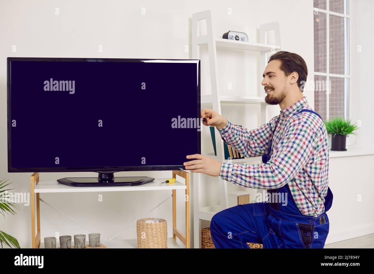Young repairman or technician fixing or installing a modern large television set at home Stock Photo