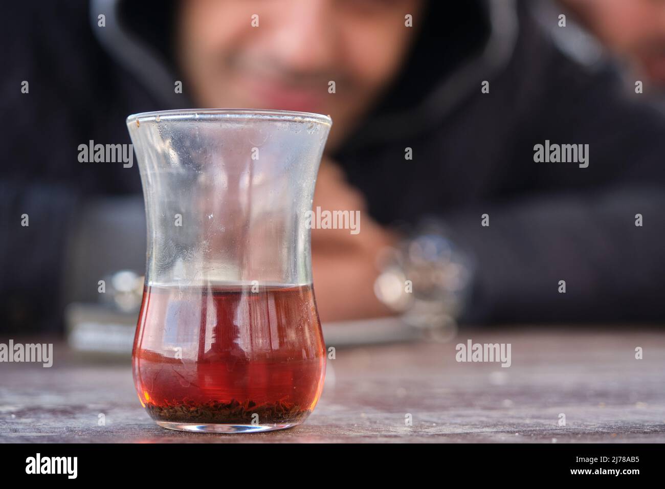 Traditional turkish tea inside traditional slim waisted glass cup, blurred smiley man photo behind the tea glass. Stock Photo