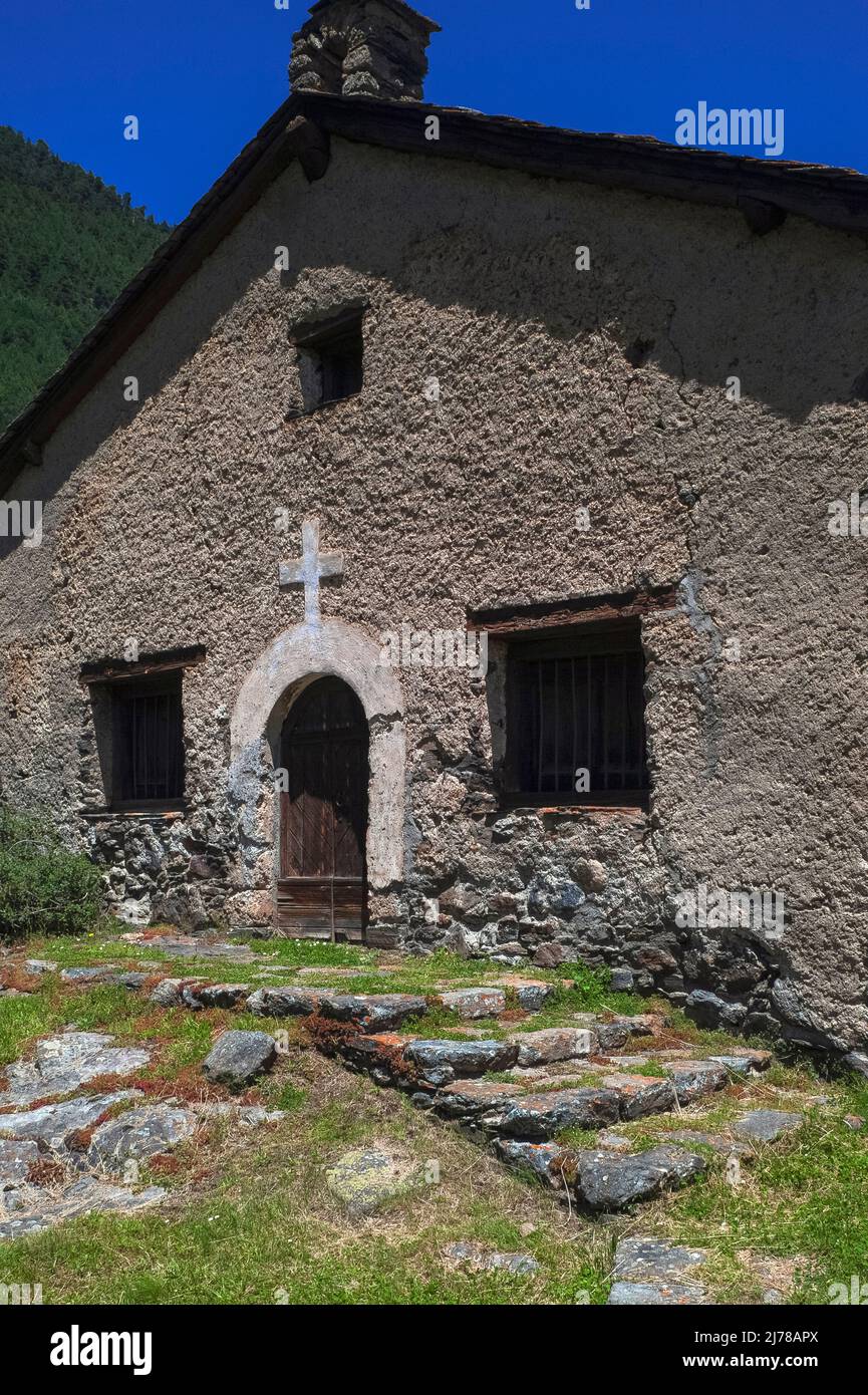 Rustic charm amid rural beauty: the simple late-16th century village church of Sant Pere del Serrat at El Serrat in the Ordino Valley, Andorra, has a round-arched doorway below a white cross, a wide gable and a small bellcote. Stock Photo