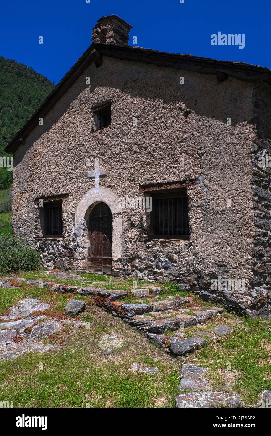 Rustic simplicity amid Pyrenean peaks: the late-16th century village church of Sant Pere del Serrat at El Serrat in the Ordino Valley, Andorra, has a round-arched doorway below a white cross, a wide gable and a small bellcote. Stock Photo