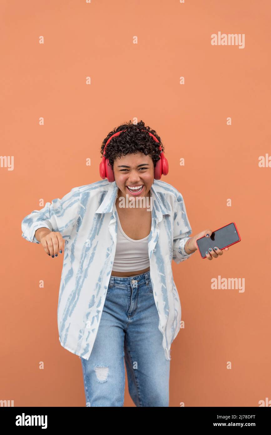 Portrait of happy young latin woman with smartphone and earphones dancing in the street, Panama, Central America Stock Photo