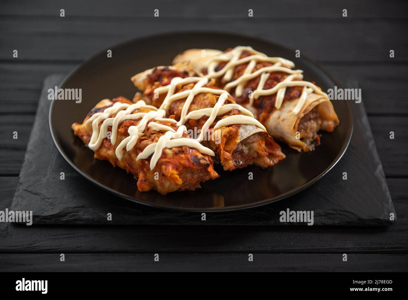 Cooked enchiladas on a black plate on a dark background. Stock Photo
