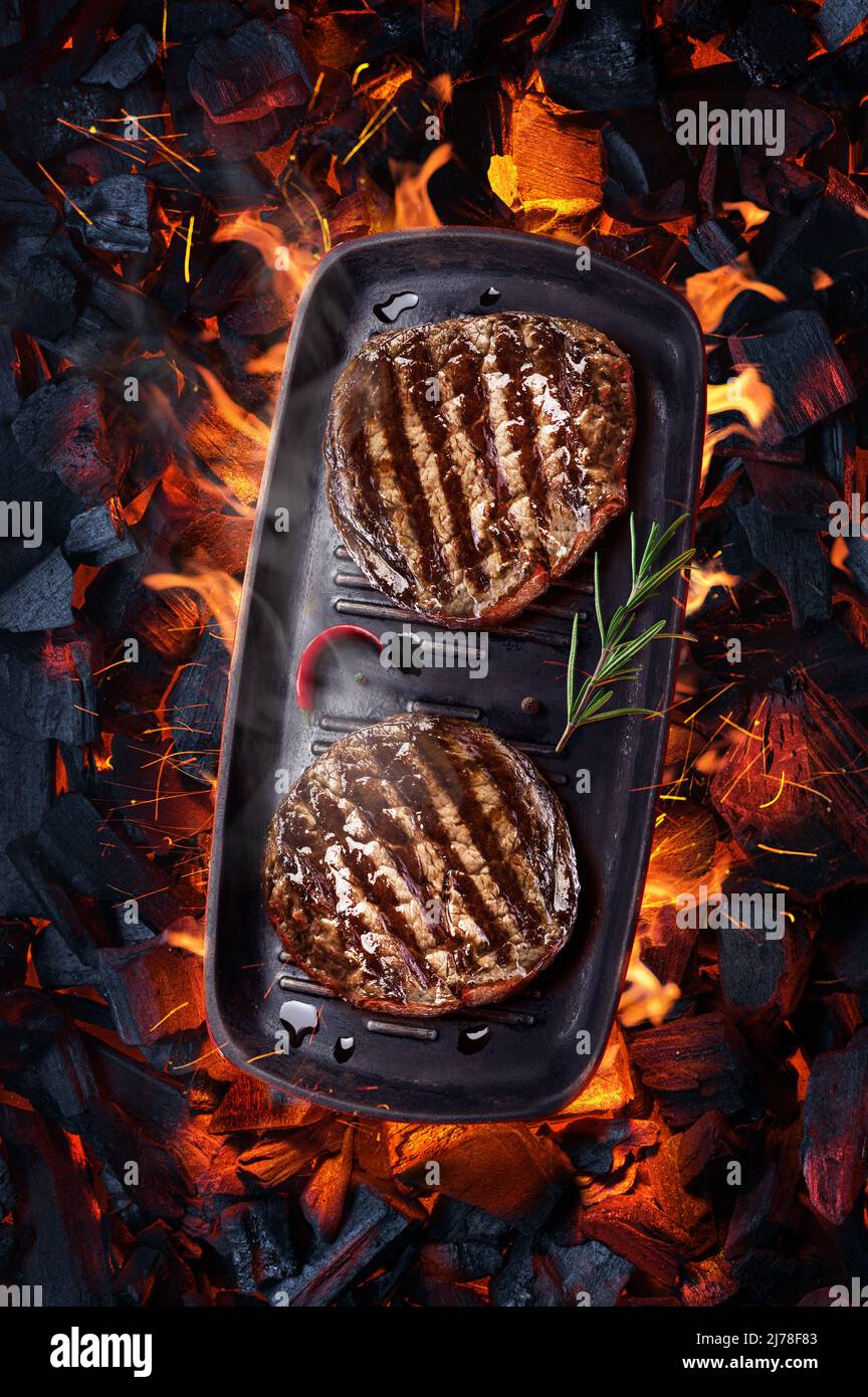 Two grilled filet mignon beef steaks on bbq pan over hot pieces of