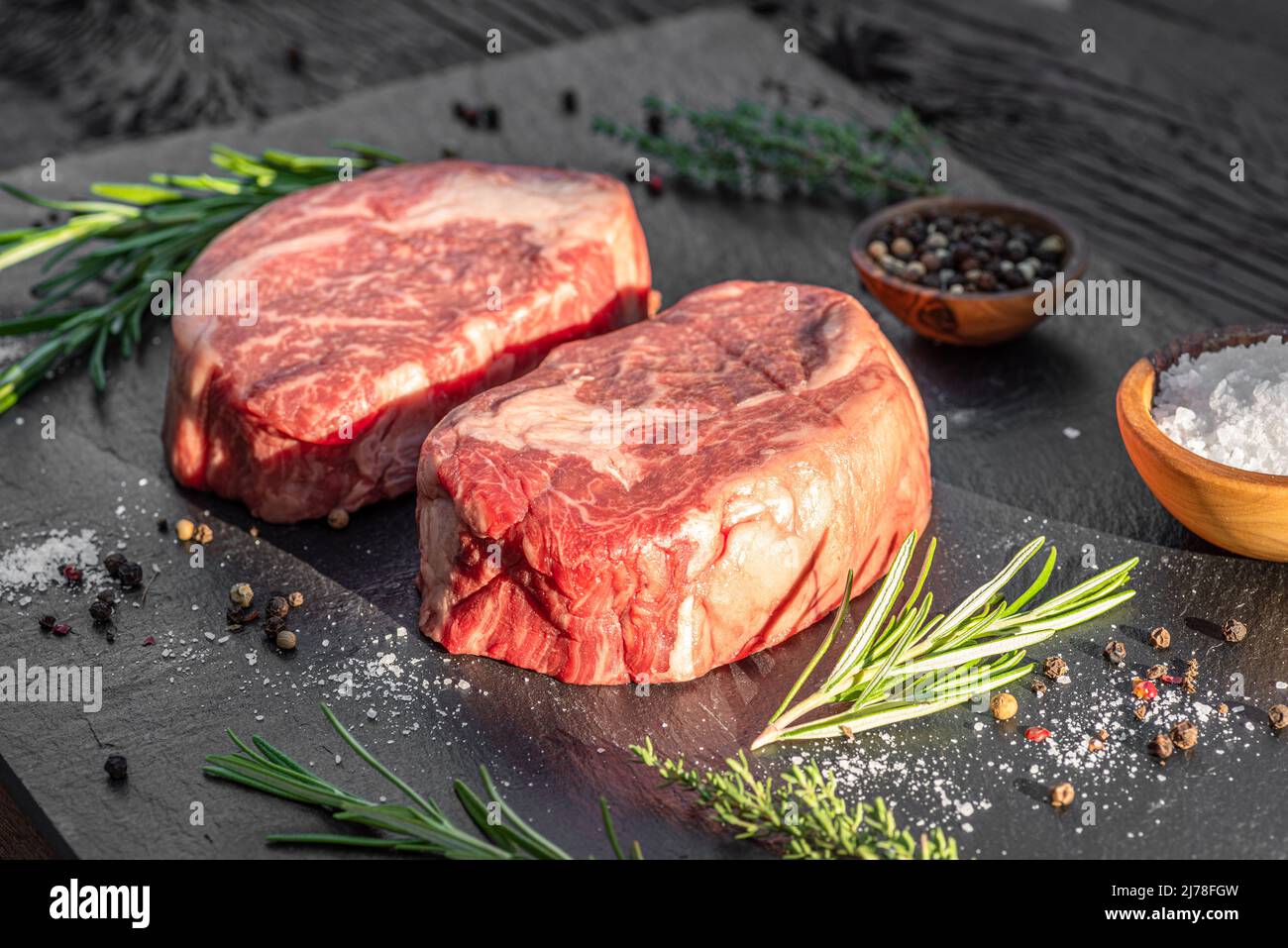 Raw Ribeye steaks with salt and herbs on grey board. Top view Stock
