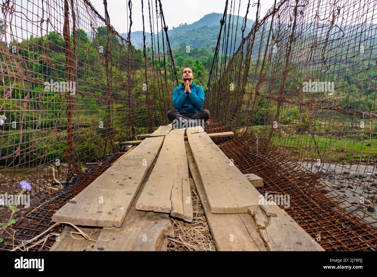 man meditating at vintage iron suspension bridge from low angle image is taken at nongjrong meghalaya india. Stock Photo