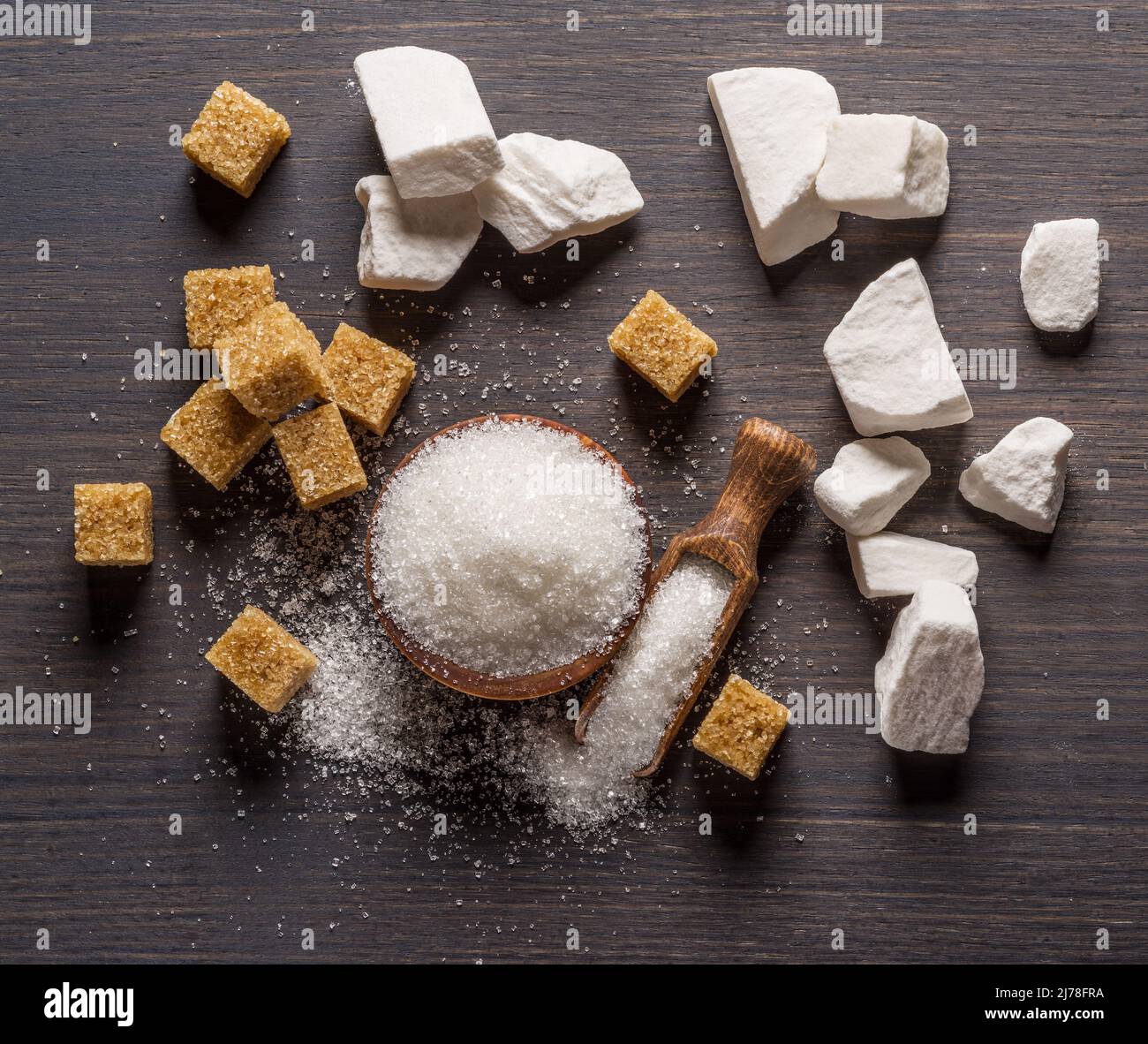 Granulated table sugar in wooden bowl and in the spoon and sugar cubes