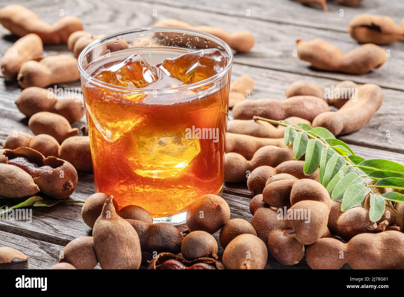 Glass of cool refreshing tamarind drink and some tamarind fruit on wooden table. Stock Photo