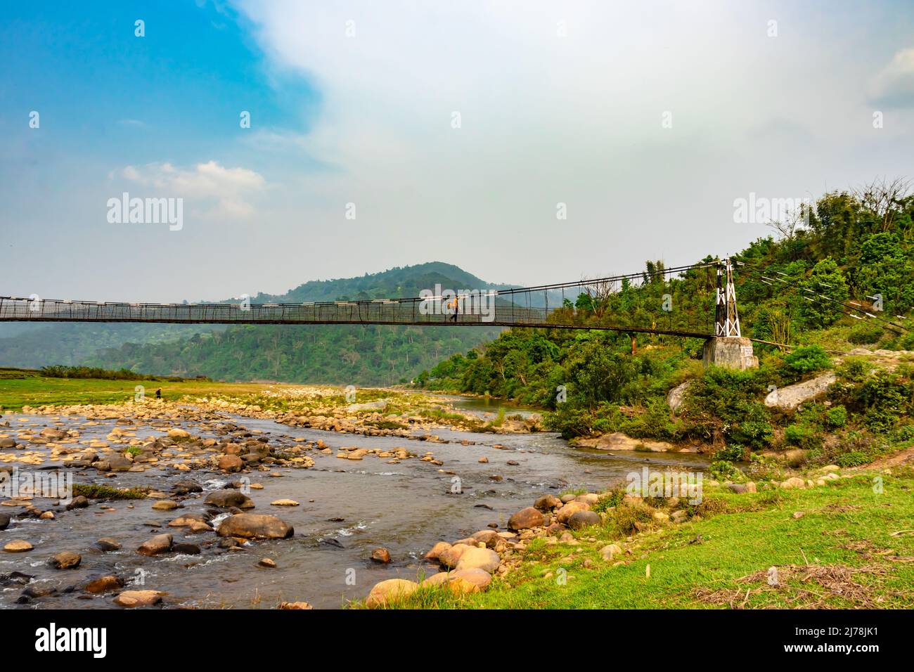 isolated iron suspension bridge over flowing river with mountain and blue sky background at morning image is taken at nongjrong meghalaya india. Stock Photo