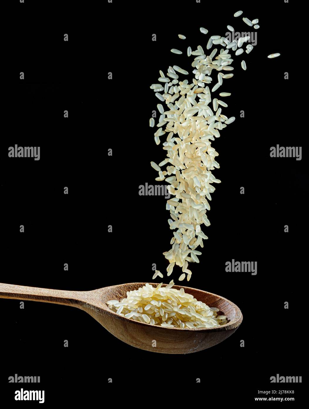 White rice grains falling down into the spoon at black background. Popular food and main