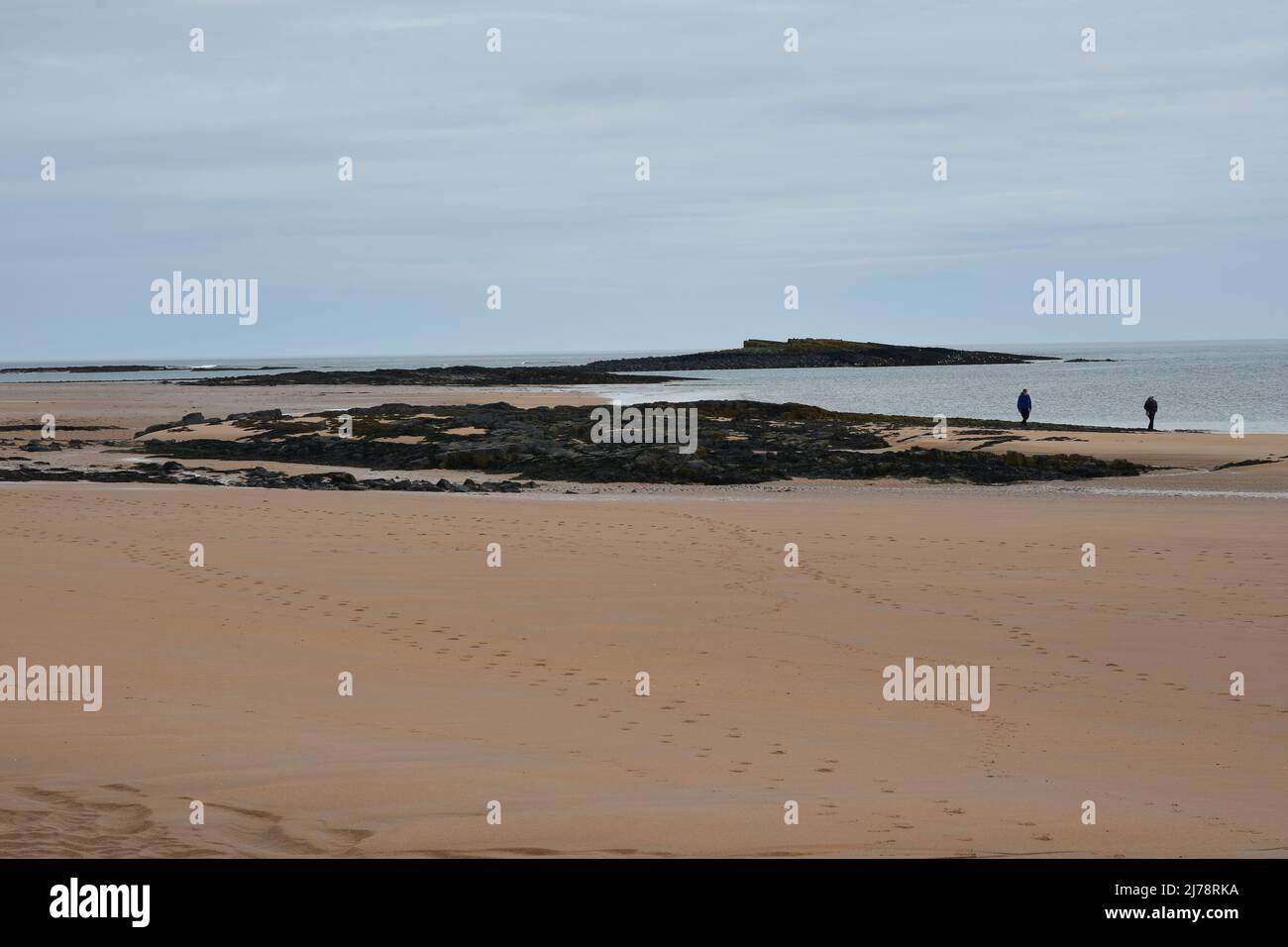 Atmospheric view of Embleton bay with a couple walking, Northumberland Stock Photo