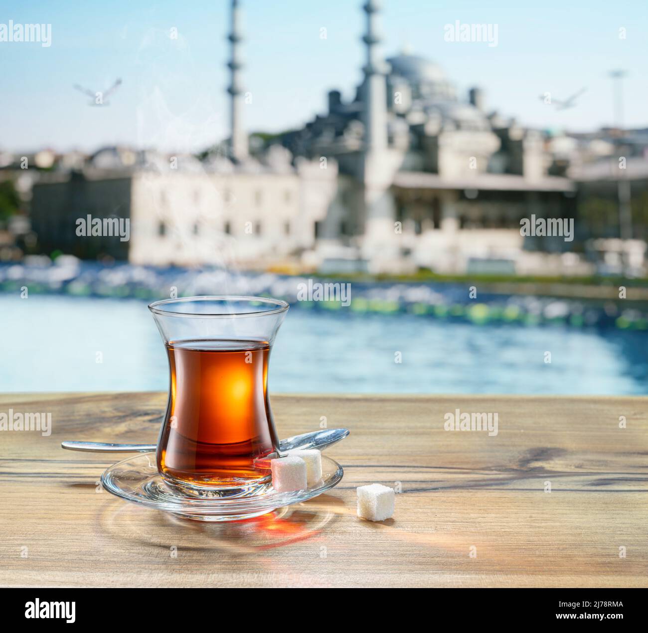 https://c8.alamy.com/comp/2J78RMA/turkish-tea-served-in-tulip-shaped-glass-on-a-small-saucer-blurred-old-town-and-sea-at-the-background-2J78RMA.jpg