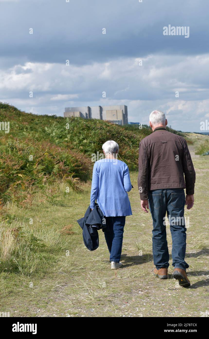 older retired man and woman walking along beach at sizewell suffolk towards sizewell A and B nuclear power station sizewell suffolk england Stock Photo