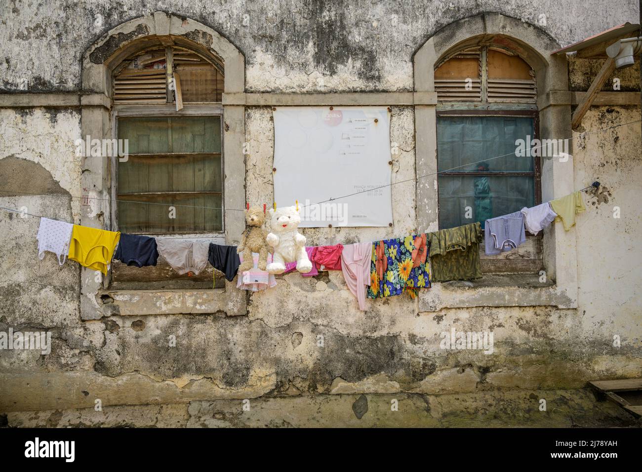 Teddy bears and clothes hung out in the sun to dry in front of a decrepit building of the old colonial plantation known as Roça Agua Ize. Stock Photo