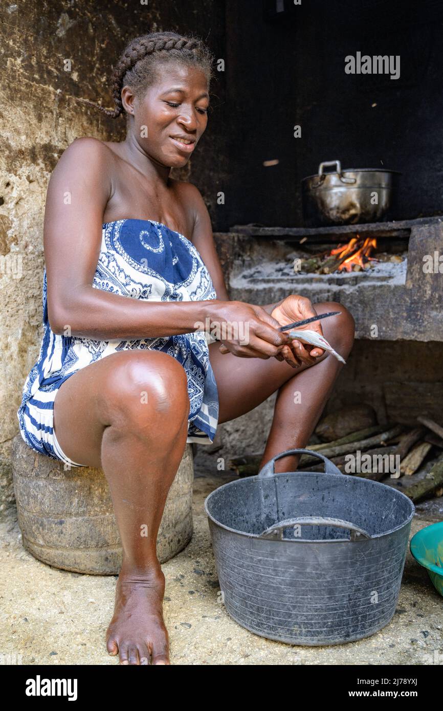 Woman cleaning fish to cook it on the fire stove of her hut. Stock Photo