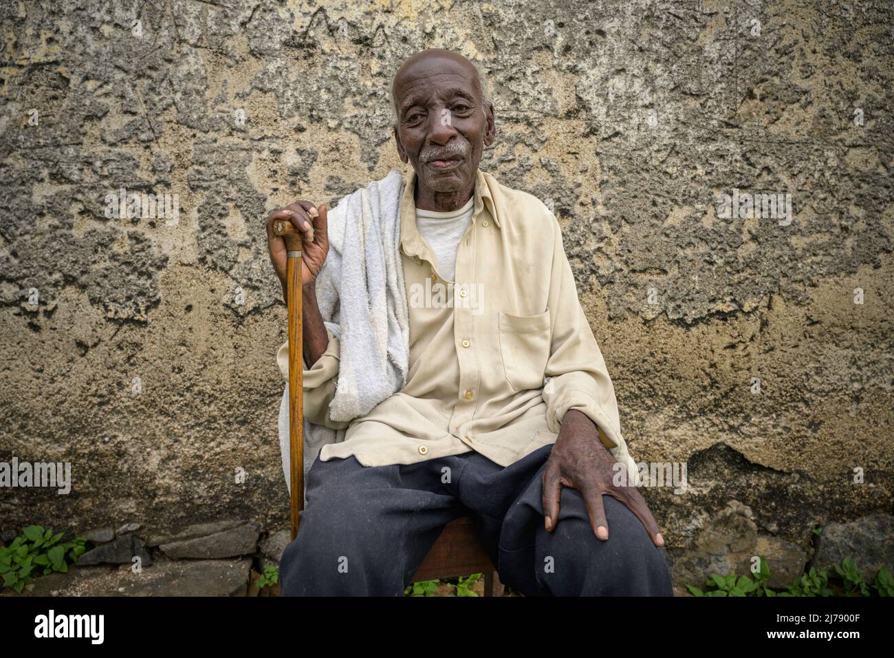 Portrait of seated African old man with walking stick. Stock Photo
