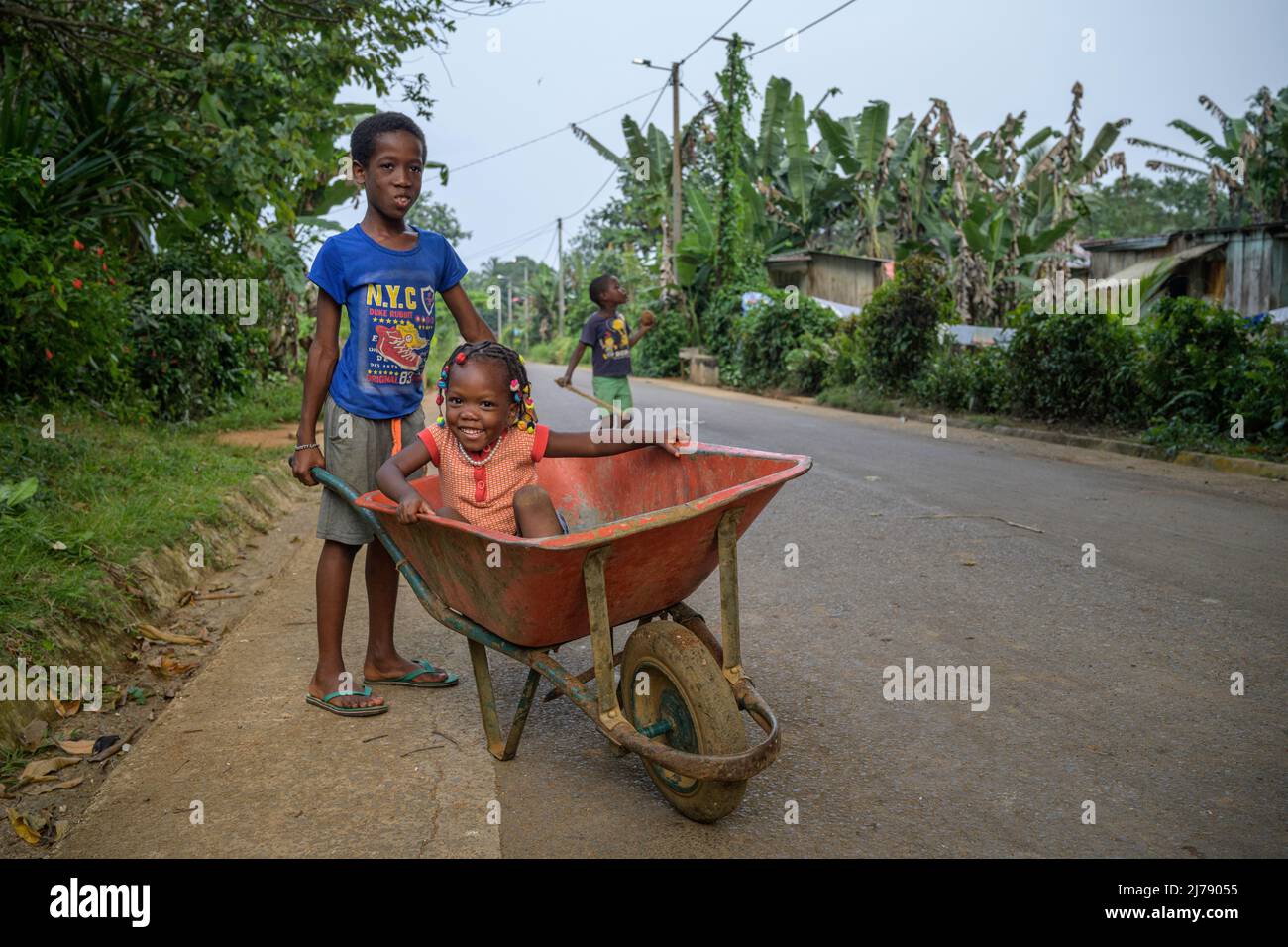 Children playing with a wheelbarrow by the road in the village of Picao. Stock Photo