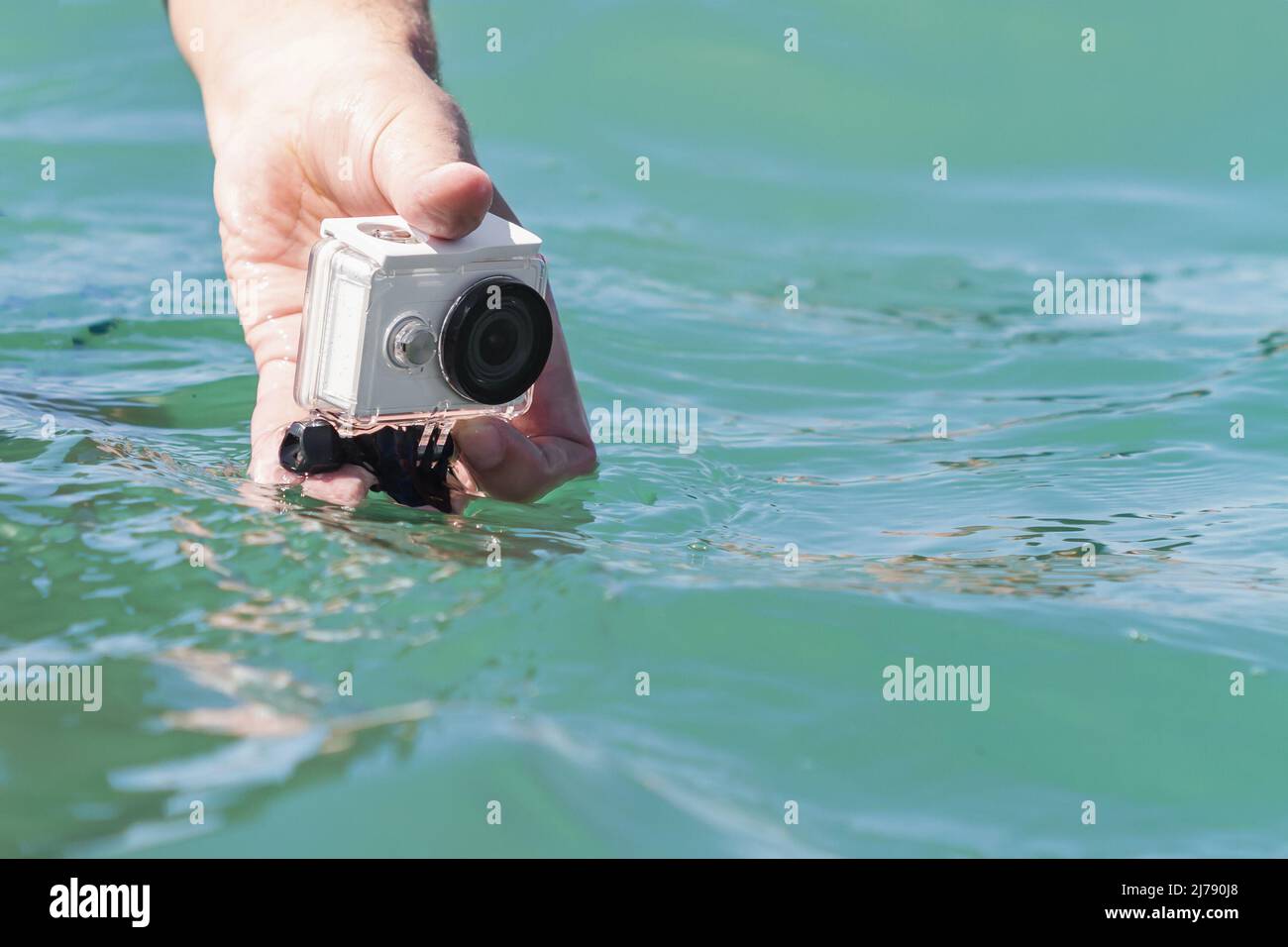 A man is taking photo and video above the water on action camera in underwater case. Closeup, selective focus Stock Photo