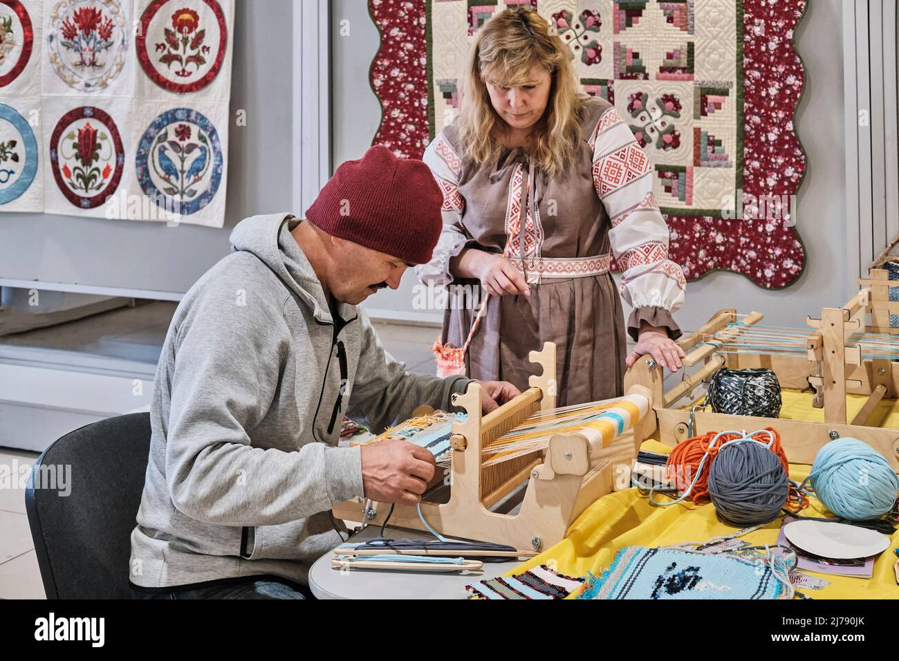 Artisan woman teaching senior asian man to weaving small rug on table loom, at masterclass on. Stock Photo