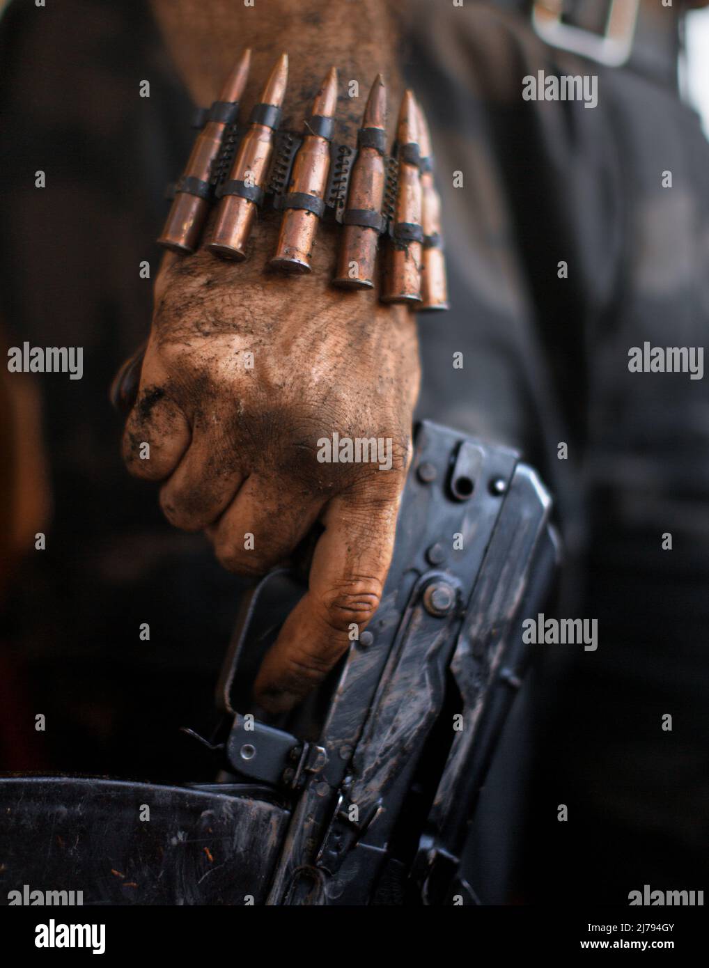 Dirty rebel hand with a machine gun and a bracelet with machine-gun cartridges. The concept of military operations, terrorism and popular resistance. Stock Photo
