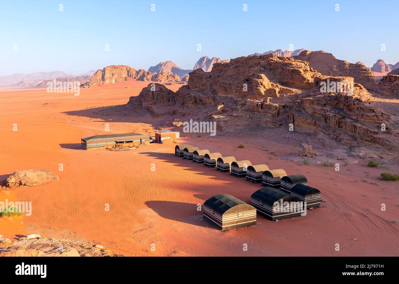 Wadi Rum desert, Jordan. Beautiful aerial view of bedouin camp at sunset from above with tents lined up and red rock formations landscape. Stock Photo
