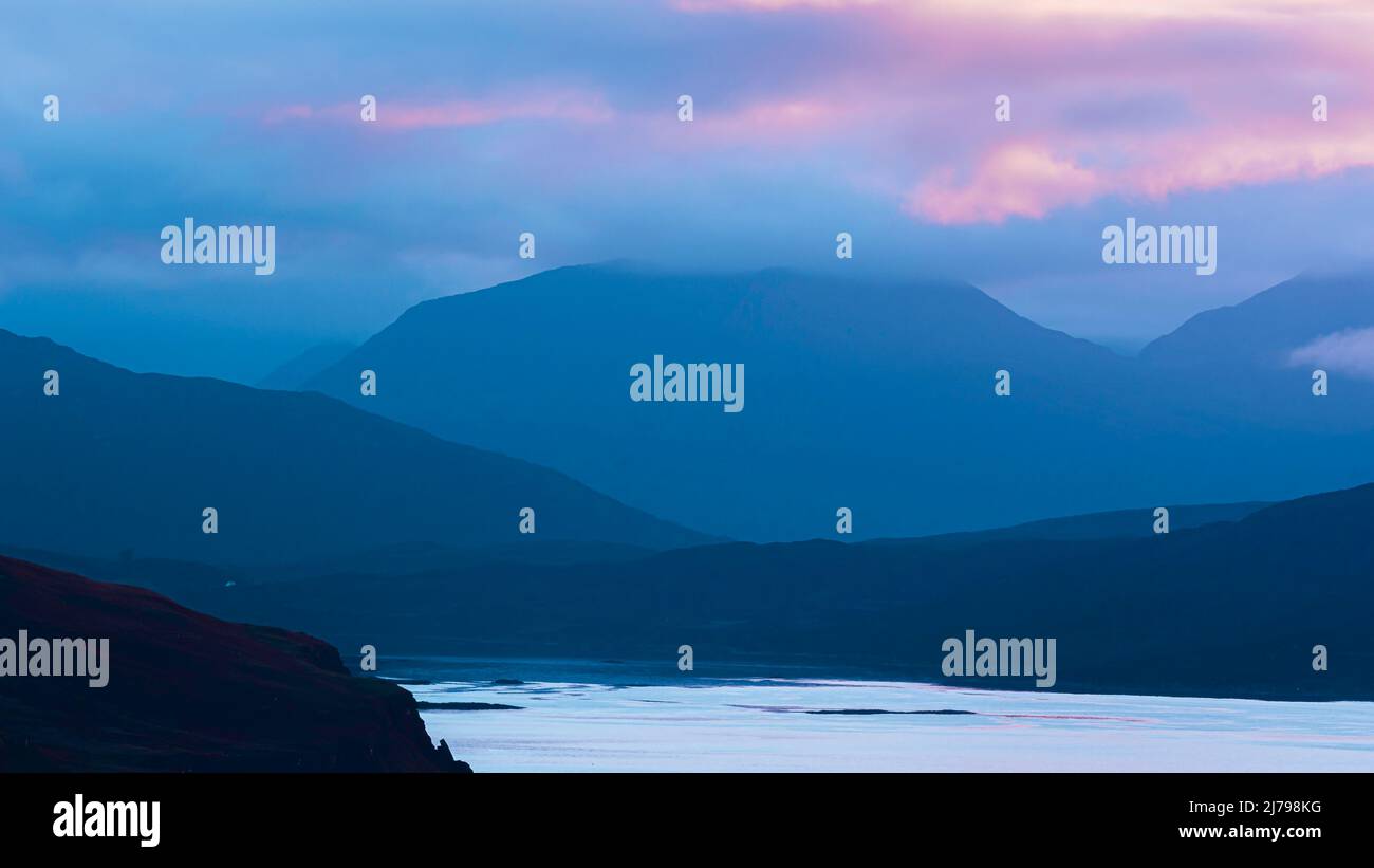 Dreamlike morning on Isle of Skye.Pink clouds over misty mountains and water.Beautiful landscape scenery in Scotland. Stock Photo