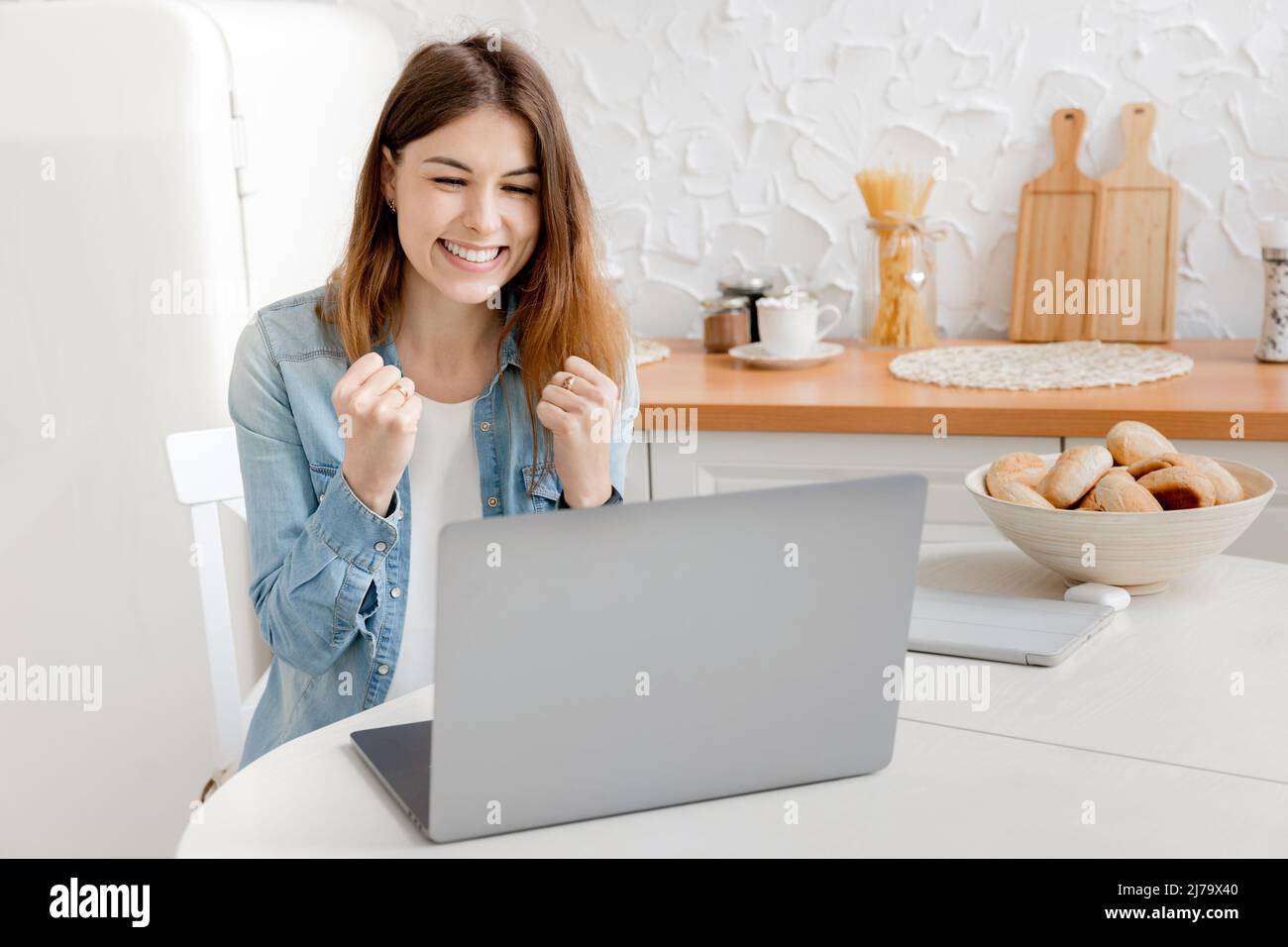 Joyful young business woman is happy about her work achievement, smiling looking at laptop. Beautiful female freelancer or student got a job promotion Stock Photo