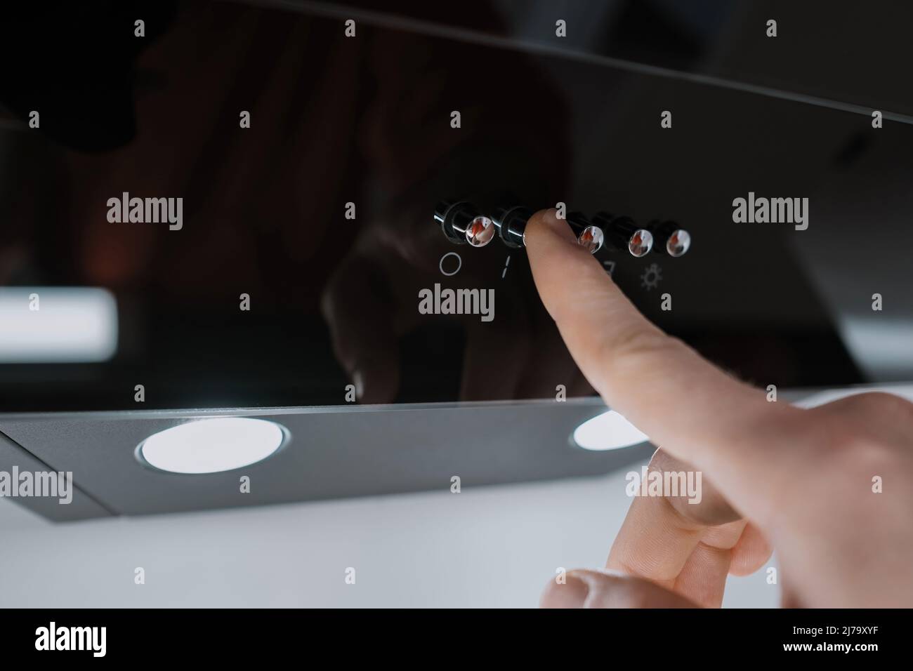 Aspirator, man pressing the buttons of a glossy black extractor hood in