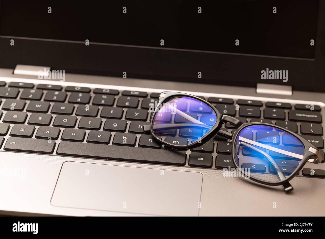 Reading glasses with coating filter to prevent Computer Vision Syndrome (CVS) sit on laptop keyboard. Concept of digital eye strain caused by screens Stock Photo