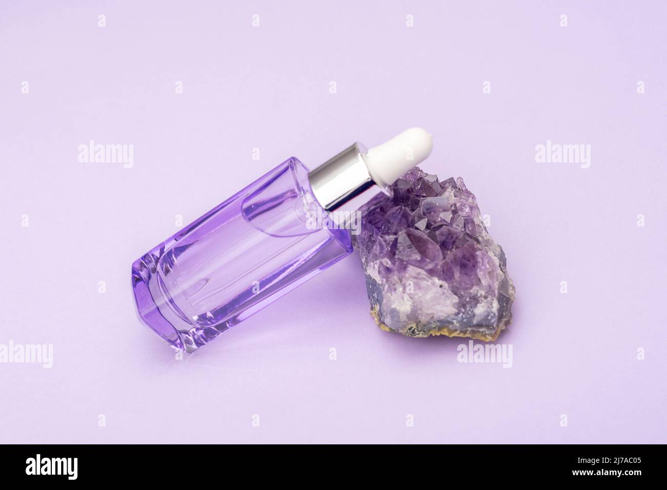 Purple cosmetic serum bottle on amethyst crystal stone, close up. Stock Photo